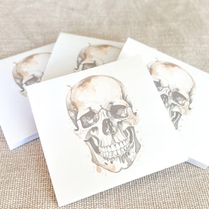 May include: A stack of white note cards with a watercolor illustration of a brown skull on the front.