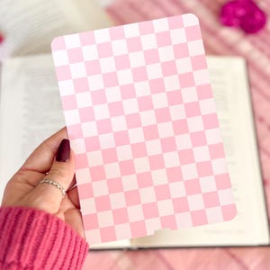May include: A pink and white checkered card with a smooth, glossy finish. The card is held in a hand with a pink sweater.