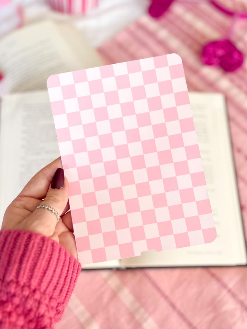 May include: A pink and white checkered card with a smooth, glossy finish. The card is held in a hand with a pink sweater.