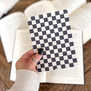 May include: A rectangular card featuring a repeating black and white checkered pattern. The card has rounded corners and a flat surface, displaying a high-contrast grid design consisting of alternating dark and light square tiles across the entire face.