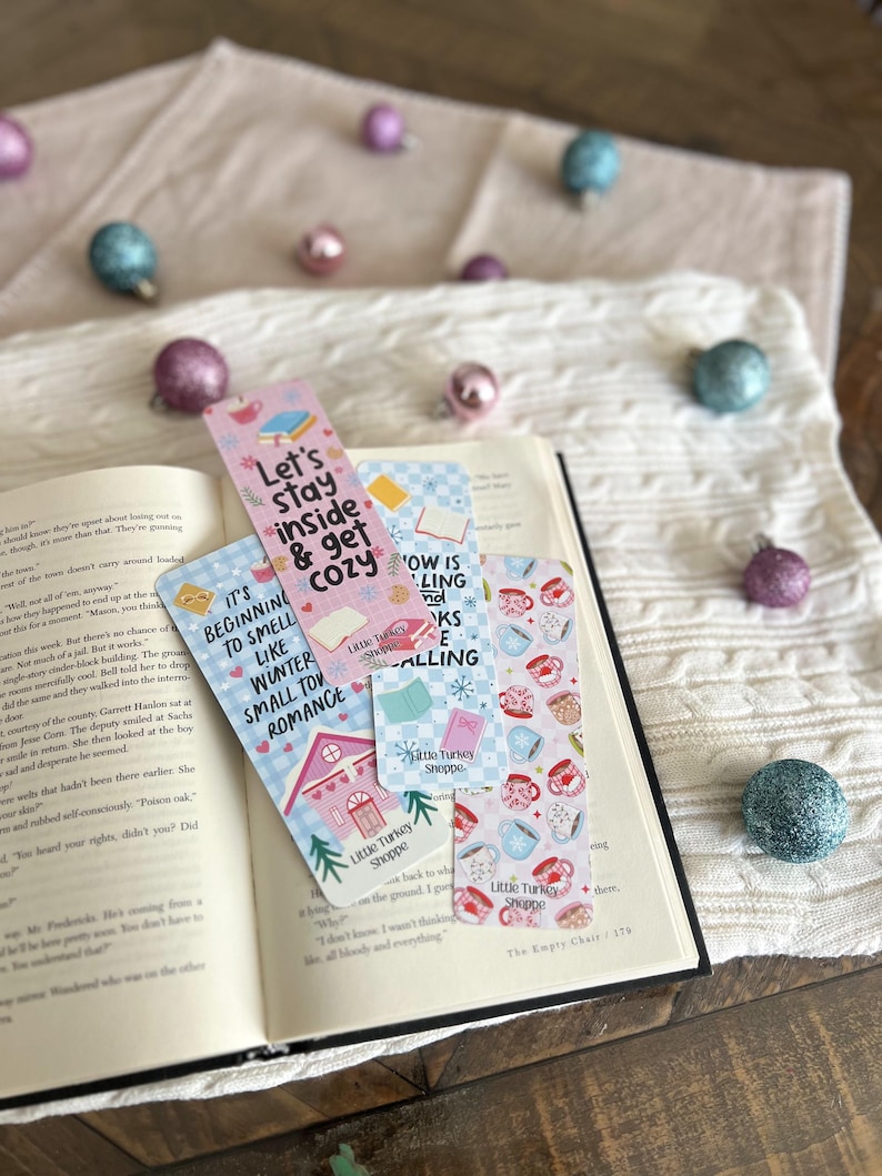 May include: Four pink and blue bookmarks with illustrations of mugs, teacups, and a small house. The bookmarks feature text that reads "Let's stay inside & get cozy", "It's beginning to smell like winter small town romance", "Now is the time for books & calling", and "Little Turkey Shoppe".