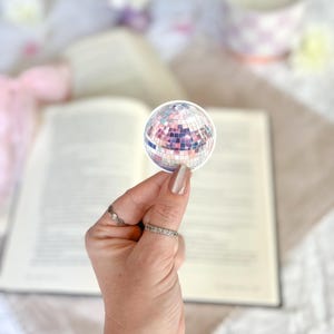 May include: A silver disco ball sticker with a pink and purple iridescent finish.