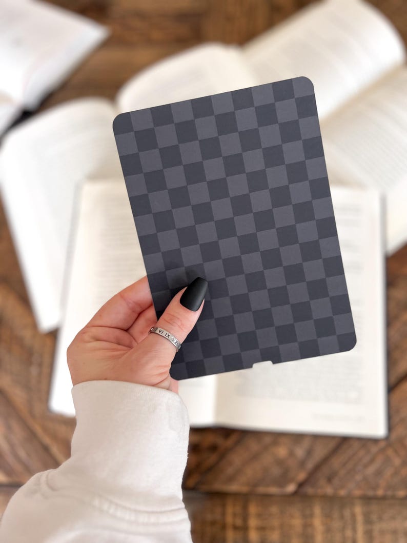 May include: A rectangular card featuring a dark gray and black checkered pattern with rounded corners. The card has a small notch at the bottom center edge and a smooth, matte finish, displaying a consistent grid design across its entire surface.