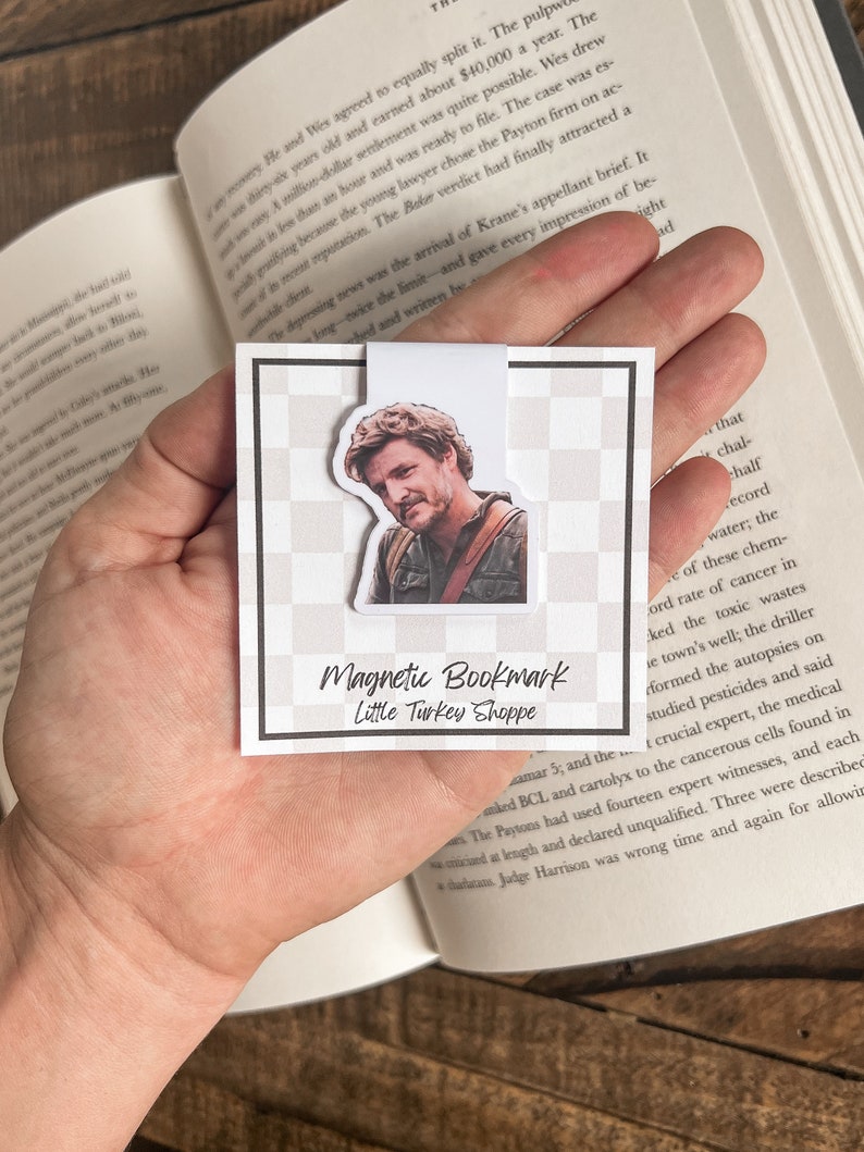 May include: A white magnetic bookmark with a black and white checkered background. The bookmark features a photo of a man with brown hair and a beard. The text "Magnetic Bookmark" and "Little Turkey Shoppe" is printed on the bookmark.
