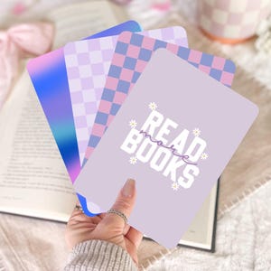 May include: A set of four purple and blue patterned cards with the text "Read More Books" on one card. The cards are held in a hand.