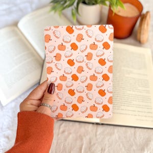 Pu&ograve; includere: Una carta rettangolare con un motivo ripetuto di zucche arancioni e girelle alla cannella glassate di bianco su sfondo rosa chiaro. Il design include piccoli punti bianchi sparsi tra le illustrazioni su tutta la superficie della carta.