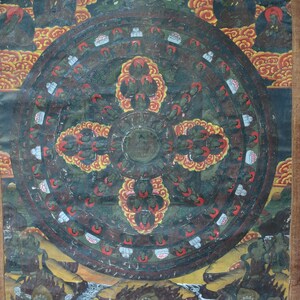 Puede incluir: Una pintura detallada y colorida que representa un diseño en forma de rueda con múltiples figuras y elementos florales. La obra de arte presenta un fondo oscuro con acentos rojos, amarillos y verdes, y está enmarcada con un borde marrón. La pintura parece ser de importancia religiosa o cultural.
