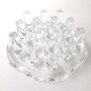 Peut inclure: Un crapaud de fleur en verre transparent avec de multiples ouvertures cylindriques. Le crapaud est en verre clair et transparent, et les ouvertures sont conçues pour maintenir les tiges de fleurs. La base est de forme arrondie.