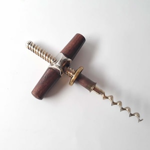 Puede incluir: Un sacacorchos vintage de madera y metal con un tornillo plateado y un mango de color latón.