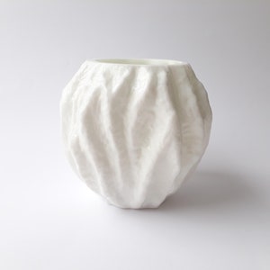 May include: A white ceramic vase with a textured, wavy surface. The vase is round and has a wide opening.