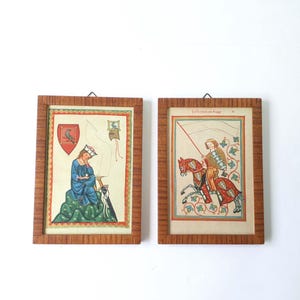 Op de afbeelding: Twee ingelijste prenten in middeleeuwse stijl. Eén toont een figuur in blauwe gewaden, de andere een ridder te paard. Beide hebben sierlijke houten frames en tonen levendige kleuren en historische beelden, geschikt voor wanddecoratie.