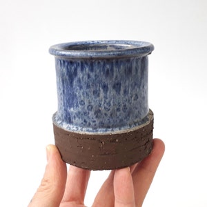 Könnte beinhalten: Ein kleiner blauer und brauner Keramiktopf mit einem gesprenkelten Überzug. Der Topf hat eine breite Basis und eine schmale Oberseite.