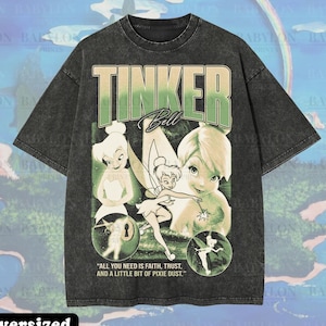 Puede incluir: Una camiseta premium de gran tamaño de color gris oscuro con un gráfico de Campanilla y el texto "TINKER Bell". El diseño incluye imágenes de Campanilla en varias poses, con la cita "ALL YOU NEED IS FAITH, TRUST, AND A LITTLE BIT OF PIXIE DUST."