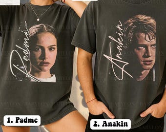 May include: Two dark gray t-shirts featuring portraits of Padme and Anakin. The Padme shirt has the name "Padme" in white script. The Anakin shirt has the name "Anakin" in white script. The shirts are labeled "Comfort Colors Pepper".