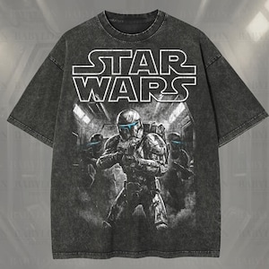 May include: A dark gray oversized t-shirt featuring a Star Wars graphic. The design includes the Star Wars logo and an illustration of characters in helmets. The shirt has the text "Oversized Premium Tee!" and "Original Artist of This Design".