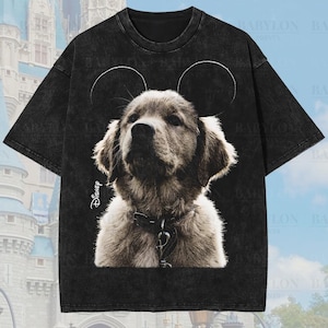 Puede incluir: Camiseta negra de gran tamaño de primera calidad con un cachorro en tonos sepia con orejas de Mickey Mouse. La camiseta tiene el logotipo de Disney y el texto "Original Artist of This Design". La camiseta está etiquetada como "Premium Wash: Black" y "Oversized Premium Tee!"