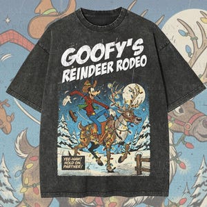 Może przedstawiać: Ciemnoszara, ponadwymiarowa koszulka premium z grafiką z kreskówki z Goofym jadącym na reniferze, z napisem "GOOFY'S REINDEER RODEO". Koszulka ma napis "YEE-HAW! HOLD ON, PARTNER!" i "Original Artist of This Design".
