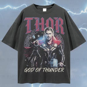 May include: Dark grey oversized t-shirt with a graphic of Thor, the God of Thunder, and the word "THOR" in red. The image shows the character holding a hammer, with the text "GOD OF THUNDER" below. The shirt is a relaxed fit.