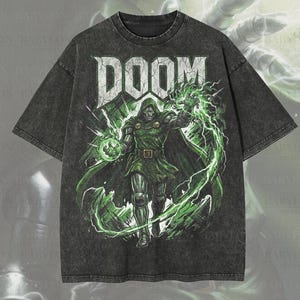 May include: Dark gray oversized premium tee featuring a graphic of a character with the word "DOOM" in white. The character is in green and black, surrounded by green lightning. The shirt has the text "Premium Wash: Pepper" and "Oversized Premium Tee!"