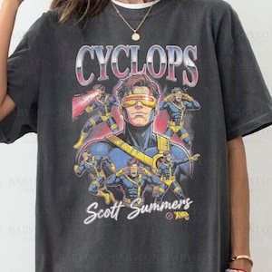 May include: Dark gray t-shirt featuring a graphic of Cyclops from X-Men. The design includes the character's name, "CYCLOPS," and "Scott Summers." The shirt is labeled "Comfort Colors" and "Pepper."