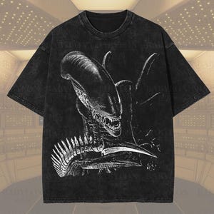 以下が含まれることがあります： プレミアムウォッシュ仕上げの黒いオーバーサイズ半袖Tシャツ。フロントには、頭部が長く鋭い歯を持つゼノモーフのクリーチャーが描かれた、大きく詳細な白いグラフィックイラストがプリントされています。Babylon Printsの文字が含まれています。