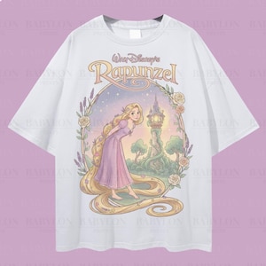 Op de afbeelding: Wit oversized T-shirt met een Rapunzel-afbeelding. Het ontwerp bevat Rapunzel in een roze jurk met lang blond haar, een toren en bloemaccenten. Het shirt heeft de tekst "Walt Disney's Rapunzel".