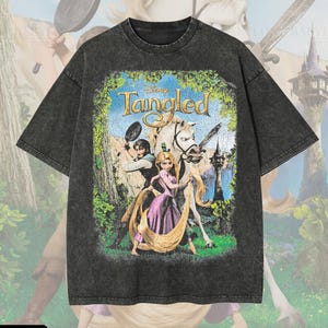 Può includere: Una t-shirt a maniche corte color grigio antracite con effetto lavaggio acido, caratterizzata da una stampa grafica del poster del film Disney Rapunzel - L'intreccio della torre. Il design mostra Rapunzel, Flynn Rider e il cavallo Maximus.