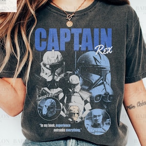 Op de afbeelding: Een donkergrijs t-shirt met de tekst "CAPTAIN Rex" in blauw, met afbeeldingen van kloontroepen. Het shirt bevat ook de quote "In my book, experience outranks everything." Het shirt is gelabeld "Comfort Colors Pepper."
