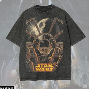 May include: Dark grey oversized t-shirt with a Star Wars graphic. The design depicts a cockpit scene with characters and the Death Star. The shirt has the text "STAR WARS" in gold and the text "Oversized Premium Tee!"
