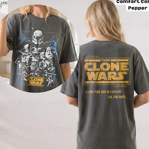 Może przedstawiać: Ciemnoszary t-shirt z krótkim rękawem z grafiką z przodu przedstawiającą postacie z Star Wars Clone Wars w kolorze niebieskim i białym. Z tyłu znajduje się żółty napis THE CLONE WARS oraz A LONG TIME AGO IN A GALAXY FAR, FAR AWAY....
