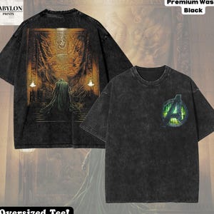 以下が含まれることがあります： ブラックのアシッドウォッシュ加工が施されたオーバーサイズTシャツ。背中には黄金のアーチ型ドアの前に立つフード付きの人物の大きなグラフィック、胸元には緑のアクセントが入ったアベンジャーズのロゴがプリントされています。テキストには「Premium Wash: Black」と記載されています。