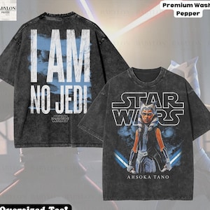 以下が含まれることがあります： 2つの特大ブラックTシャツ。1つは「I AM NO JEDI」のテキストと青い雲の背景、スターウォーズのロゴが特徴です。もう1つのシャツは、ライトセーバーとスターウォーズのロゴを持つアソーカ・タノを表示しています。シャツはペッパーウォッシュです。