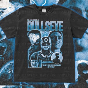 Puede incluir: Camiseta negra con un diseño gráfico azul que presenta la palabra "BULLSEYE" y retratos de personajes. La camiseta también incluye el texto "YOU DON'T KNOW WHAT I'M CAPABLE OF BUT YOU WILL." La camiseta es de Babylon Prints.