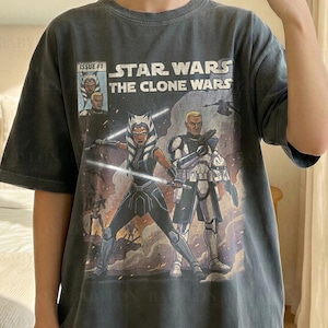 May include: A dark gray t-shirt featuring a Star Wars: The Clone Wars comic book cover. The shirt displays the text "STAR WARS THE CLONE WARS" and "ISSUE #1". The model is wearing a size XL. The shirt is labeled "Comfort Colors Pepper".