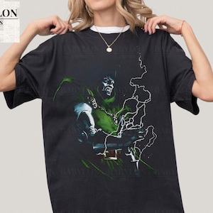 May include: Black t-shirt featuring a graphic of a comic book character in green and silver armor, with a green cape and a chain around the neck. The shirt has the text "BABYLON PRINTS" in white on the upper left.