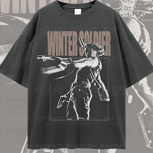 May include: A dark grey t-shirt featuring a white graphic print of a character from the Marvel Cinematic Universe. The graphic depicts the character holding a weapon and the text "Winter Soldier".