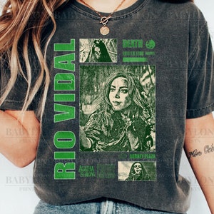 May include: A dark gray t-shirt with a green graphic print featuring a portrait of actress Aubrey Plaza as the character Agatha Harkness from the Marvel series "WandaVision". The graphic also includes the text "Rio Vidal" and "Death &  Destruction: WandaVision Marvel".