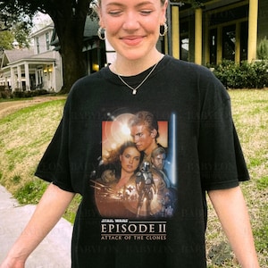 May include: A black t-shirt with a Star Wars Episode II: Attack of the Clones graphic print. The graphic features a scene from the movie with Anakin Skywalker, Padmé Amidala, and Obi-Wan Kenobi.