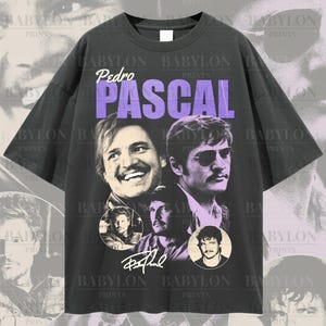 Puede incluir: Camiseta negra de gran tamaño con un estampado gráfico de la cara de Pedro Pascal en un círculo morado. El texto "Pedro Pascal" está impreso en morado encima de la imagen. La camiseta tiene cuello redondo y mangas cortas.