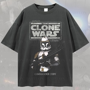 May include: A black oversized t-shirt with a vintage-style graphic of a Star Wars Clone Wars character, Commander Cody, with the text "Star Wars The Clone Wars" above him. The shirt has a distressed look and is made of a soft, comfortable fabric.