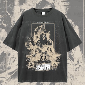 May include: An oversized t-shirt in dark grey with a graphic print of a scene from the film "Star Wars: Revenge of the Sith". The graphic has a vintage style with a faded, distressed look. The text "Revenge of the Sith" is printed in white on the graphic.