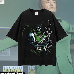 May include: Black oversized t-shirt with a graphic print of Doctor Doom from Marvel Comics. The print features Doctor Doom in a green and silver suit with a cape, holding his hands up in a gesture of power. The t-shirt has the text "Oversized Tee!" printed on the bottom.