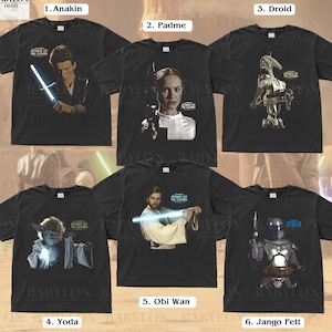 May include: Six black t-shirts featuring different Star Wars characters from the film Attack of the Clones. The characters are Anakin Skywalker, Padme Amidala, a droid, Yoda, Obi Wan Kenobi, and Jango Fett.