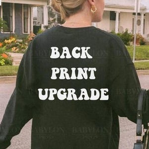 Puede incluir: Sudadera negra con las palabras "BACK PRINT UPGRADE" en letras blancas en la espalda. La sudadera es de cuello redondo. El logotipo de la marca "BABYLON PRINTS" está en la esquina superior izquierda.