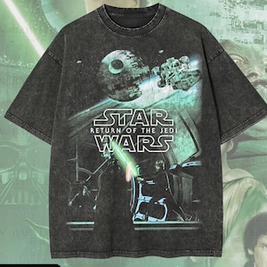 Puede incluir: Una camiseta gris oscuro de gran tamaño con un gráfico de Star Wars. El diseño incluye el texto "STAR WARS RETURN OF THE JEDI" e imágenes de personajes y naves espaciales. La camiseta tiene el texto "Oversized Premium Tee!" y "Original Artist of This Design".