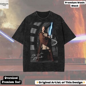 Może przedstawiać: Czarny, duży t-shirt premium z grafiką Obi-Wana Kenobiego trzymającego miecz świetlny. Obraz zawiera tekst "Obi-Wan Kenobi" i "Original Artist of This Design". Koszulka ma pranie premium.