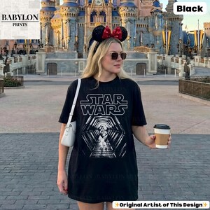 May include: Black Star Wars t-shirt with a white graphic of a tunnel and the Star Wars logo. The shirt is worn by a person in front of a castle. The text "BABYLON PRINTS" is in the upper left corner.