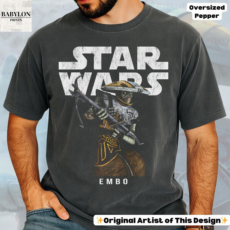 Puede incluir: Camiseta gris oscuro de gran tama&ntilde;o con un dise&ntilde;o de Star Wars. El dise&ntilde;o incluye el logotipo de Star Wars en blanco, una ilustraci&oacute;n de personaje y el nombre "EMBO" en blanco. La camiseta est&aacute; hecha de un material suave.