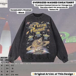 May include: Black oversized washed sweatshirt featuring a Pizza Planet graphic. The design includes the Pizza Planet logo, aliens, a rocket ship, and a planet with rings. The sweatshirt is made of premium washed cotton for a vintage look. Unisex fit.