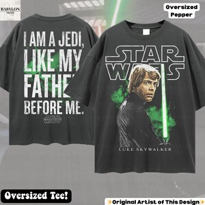 May include: Dark gray oversized t-shirt featuring Luke Skywalker with a green lightsaber and the Star Wars logo. The back of the shirt displays the text "I AM A JEDI, LIKE MY FATHER BEFORE ME." The shirt is labeled "Oversized Tee!"